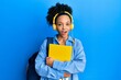 © Krakenimages.com - Young african american girl wearing student backpack and headphones holding book afraid and shocked with surprise and amazed expression, fear and excited face.