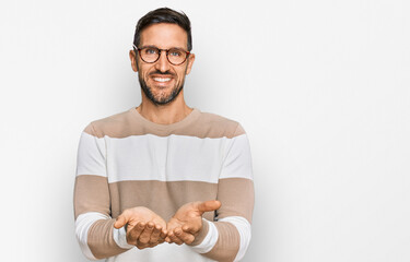 Handsome man with beard wearing casual clothes and glasses smiling with hands palms together receiving or giving gesture. hold and protection