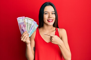 Poster - Young hispanic girl holding indian rupee banknotes smiling happy pointing with hand and finger