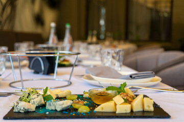 Assorted snacks on a black stone plate on a restaurant table on a window background