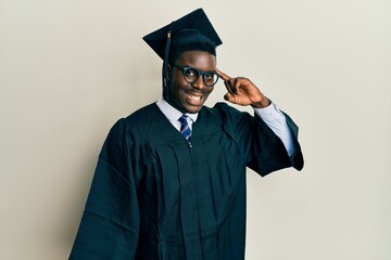 Wall Mural - Handsome black man wearing graduation cap and ceremony robe smiling pointing to head with one finger, great idea or thought, good memory