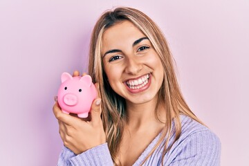 Sticker - Beautiful hispanic woman holding piggy bank smiling with a happy and cool smile on face. showing teeth.