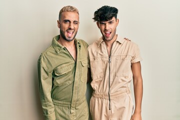 Wall Mural - Homosexual gay couple standing together wearing casual jumpsuit winking looking at the camera with sexy expression, cheerful and happy face.