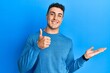 © Krakenimages.com - Hispanic young man wearing casual winter sweater showing palm hand and doing ok gesture with thumbs up, smiling happy and cheerful