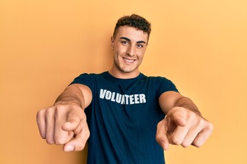 Hispanic young man wearing volunteer t shirt pointing to you and the camera with fingers, smiling positive and cheerful