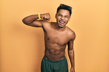 Young african american man wearing swimwear and swimmer glasses angry and mad raising fist frustrated and furious while shouting with anger. rage and aggressive concept.