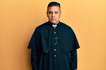 Canvas Print - Young latin priest man standing over yellow background relaxed with serious expression on face. simple and natural looking at the camera.