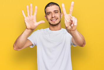 Hispanic young man wearing casual white t shirt showing and pointing up with fingers number seven while smiling confident and happy.