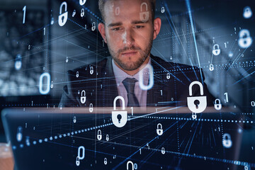 Handsome businessman in suit at workplace working with laptop to defend customer cyber security. Concept of clients information protection and brainstorm. Padlock hologram over office background.