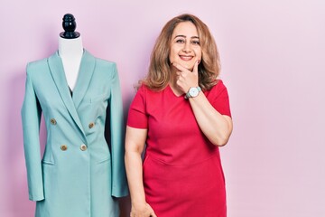 Poster - Middle age caucasian woman standing by manikin looking confident at the camera smiling with crossed arms and hand raised on chin. thinking positive.