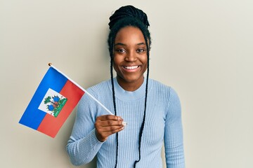 Poster - African american woman with braided hair holding haiti flag looking positive and happy standing and smiling with a confident smile showing teeth