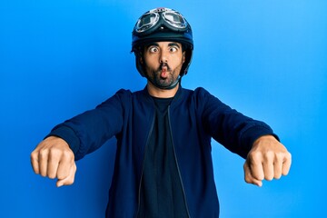 Canvas Print - Young hispanic man holding motorcycle helmet making fish face with mouth and squinting eyes, crazy and comical.