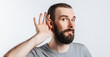 © Daria Lukoiko - Handsome young man holds his hand near his ear, wants to hear better on a white background with a place for advertising mockup