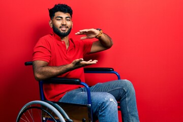 Canvas Print - Arab man with beard sitting on wheelchair gesturing with hands showing big and large size sign, measure symbol. smiling looking at the camera. measuring concept.