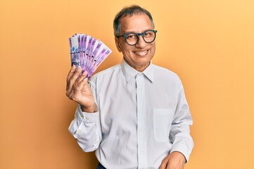 Poster - Middle age indian man holding 100 philippine peso banknotes looking positive and happy standing and smiling with a confident smile showing teeth