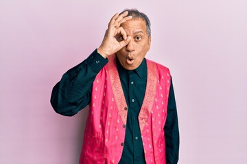 Canvas Print - Middle age indian man wearing traditional indian clothes doing ok gesture shocked with surprised face, eye looking through fingers. unbelieving expression.