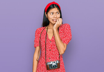 Poster - Beautiful young asian woman wearing dress and vintage camera looking stressed and nervous with hands on mouth biting nails. anxiety problem.