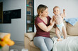 © Drazen - Baby boy standing on the sofa with help of his mother at home.