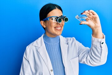 Sticker - Beautiful brunette jeweller woman holding brilliant diamond stone wearing magnifier glasses smiling with a happy and cool smile on face. showing teeth.