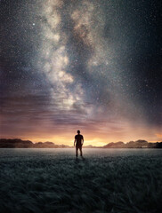 Wall Mural - a man exploring the night sky as the milky way galaxy fills the landscape from above. photo composit