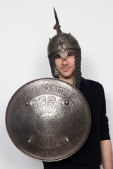 Young guy is posing in studio with helmet and shield. Knight, halloween concept.