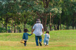 © Mongkolchon - grand father holding hands of grandchildren walking together in park