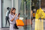 Fototapeta  - Asian woman using the smart mobile phone for check online shopping order is completed with clothes beside the glassess in store shop with happy action at department center