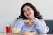 © Bangkok Click Studio - Closeup shot of Asian young happy beautiful friendly overweight fat chubby female sit relax smiling look at camera behind table with red sweet water popcorn donut and cake in blurred foreground
