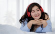 © Bangkok Click Studio - Asian young happy calm fat overweight woman lay down with happy smiling deep emotion peacefully while listening to music from big red earphones use playlist from black tablet at home in bedroom