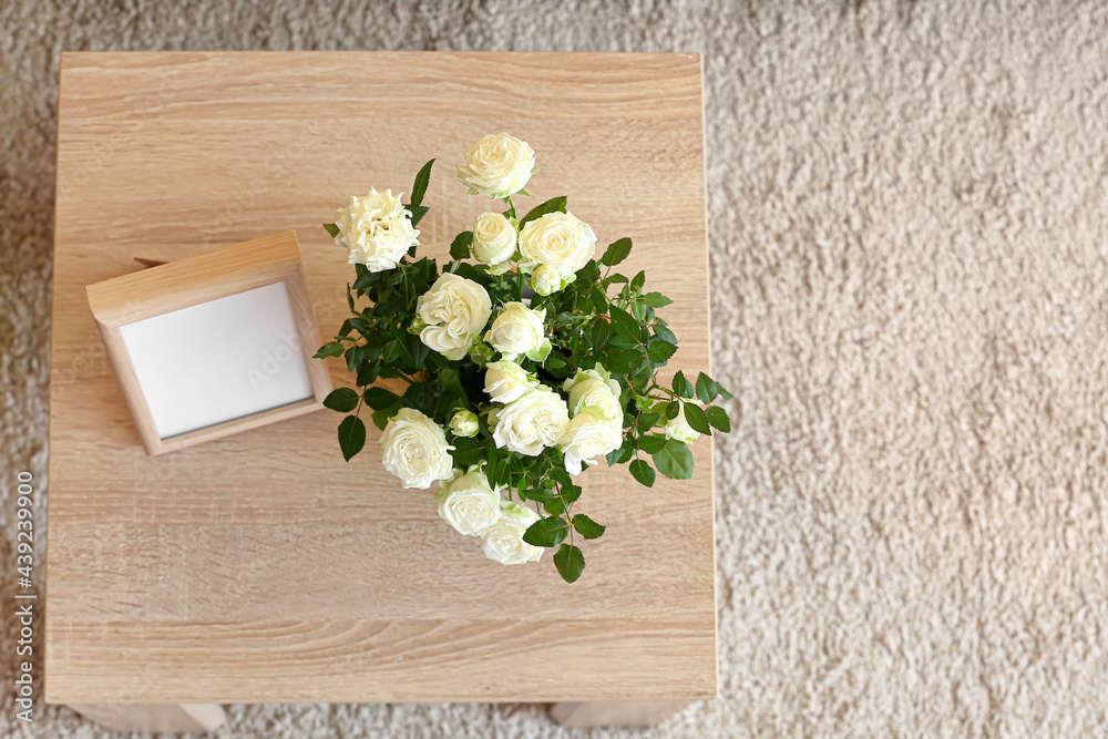 Beautiful white roses in pot and frame on table in room