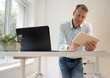 © epiximages - business man with blue shirt is standing behind high standing table and is working with his tablet