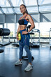 © nazarovsergey - Fit brunette woman standing with water bottle in gym