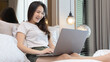 © Puwasit Inyavileart - Asian woman uses laptop on bed in modern bedroom at home after she wakes up in the morning, Entertaining or relaxing using laptop technology, Wake-up activities, Happy lifestyle.