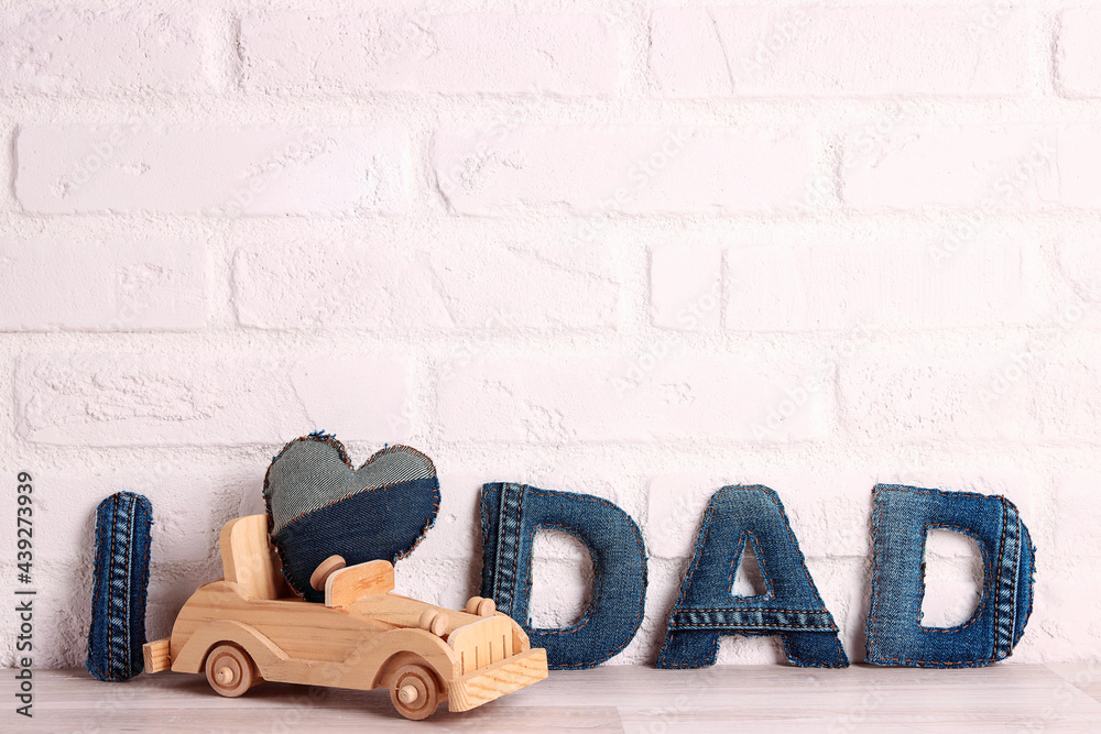 Father's day message from denim letters with wooden toy car on a white brick wall background. - obrazy, fototapety, plakaty 