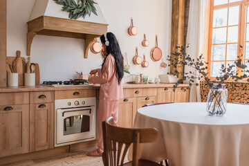 young asian woman in pink silk pajamas and headphones cooking breakfast near table in kitchen