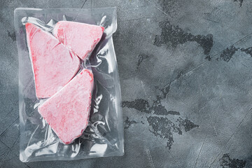 Raw frozen tuna fillet in vacuum packaging, on gray stone background, top view flat lay , with copyspace  and space for text