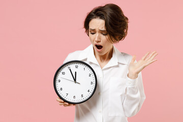 Wall Mural - Young sad displeased employee business secretary woman corporate lawyer in classic formal white shirt work in office hold clock spread hands isolated on pastel pink color background studio portrait.