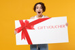 © ViDi Studio - Young surprised shocked amazed excited woman 20s in white tank top shirt hold big gift certificate coupon voucher card for store isolated on yellow background studio portrait People lifestyle concept