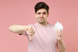 © ViDi Studio - Sick ill allergic man has watery red eyes runny nose suffer from allergy symptoms hold paper napkin look sadly camera show thumb down dislike gesture isolated on pastel pink color background studio