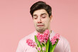 © ViDi Studio - Sick ill allergic man has red eyes runny stuffy sore nose suffer from pollen allergy symptoms hay fever hold blooming flower plant reaction on trigger isolated on pastel pink color background studio.