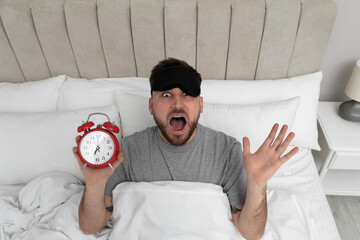 Canvas Print - Emotional overslept man with alarm clock in bed, above view. Being late concept