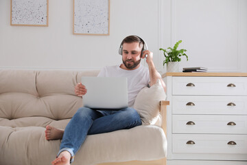 Wall Mural - Man with laptop and headphones sitting on sofa at home