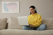 © New Africa - Woman with laptop and headphones sitting on sofa at home