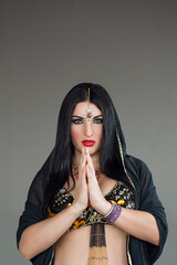 Poster - portrait of a beautiful young brunette woman dressed as an oriental beauty who dances a belly dance on a gray background