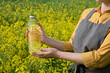 A woman stands in a rape field and holds a bottle of rapeseed oil in his hands. Concept of canola oil production.