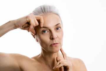 Wall Mural - Senior woman lifting skin with her hands and looking to the camera calmly