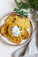 Wall Mural - Vegetable fritters or pancakes with yoghurt or cream sour dressing and herbs. Cabbage or zucchini fritters on ceramic plate. Healthy vegetarian food. Top view.