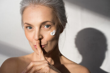 Wall Mural - Calm woman with moisturizing cream at her chick putting a finger to her lips