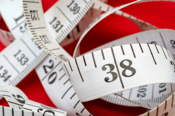 White measuring tape on red background. Measurement of length and circumference. Lose weight and get fat.