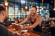 © gstockstudio - Charming young bartender in apron serving beer and smiling while working in the pub